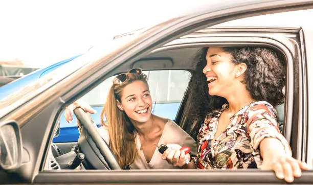 Young female best friends having fun at car roadtrip moment - Transportation concept and urban ordinary life with women girlfriends at happy travel vacation on the road - Bright azure filter