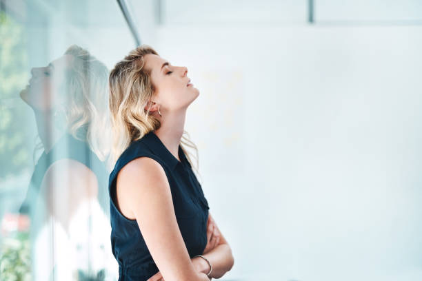 Trying to drag herself out of the doom and gloom Shot of a young businesswoman looking stressed out in an office banging your head against a wall stock pictures, royalty-free photos & images