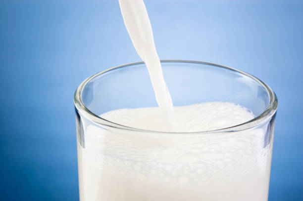 pouring fresh milk into glass on a blue background - drink close up dairy product flowing imagens e fotografias de stock