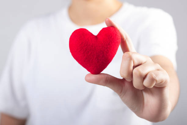 istock Woman's hand with white t-shirt holding red fabric heart shaped 1129129437