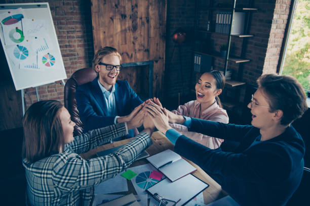 istock Four nice chic elegant stylish cheerful glad ecstatic business sharks experts gathering appointment putting hands over desktop charts at modern industrial loft interior work place station 1129129521