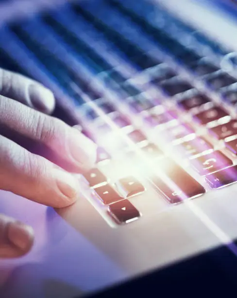 Photo of Closeup of male hands typing on laptop keyboard at the office. Visual effects, flares.