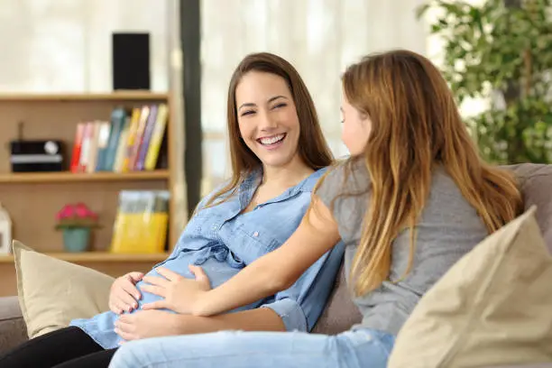 Photo of Pregnant woman talking with a friend who touches her belly