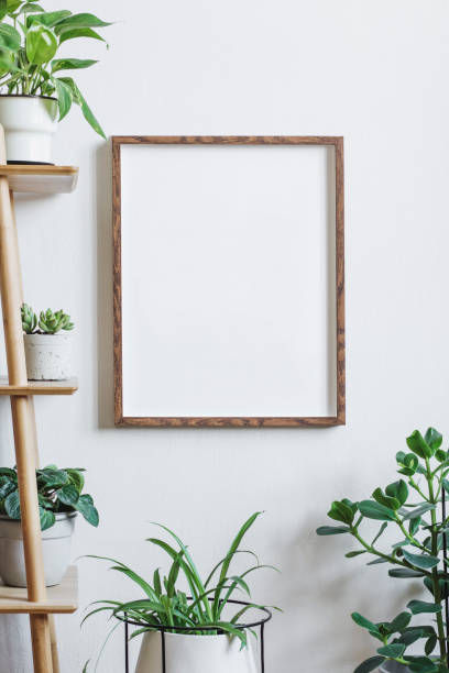 istock Scandinavian and botanical interior with brown mock up poster frame on the white wall. White backgrounds walls. Modern and floral concept. Nature lover. 1129151920