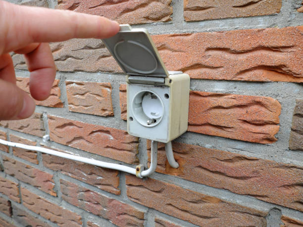 Outdoor electrical socket with child protection and the cover lifted by man's finger is mounted on the brick wall stock photo