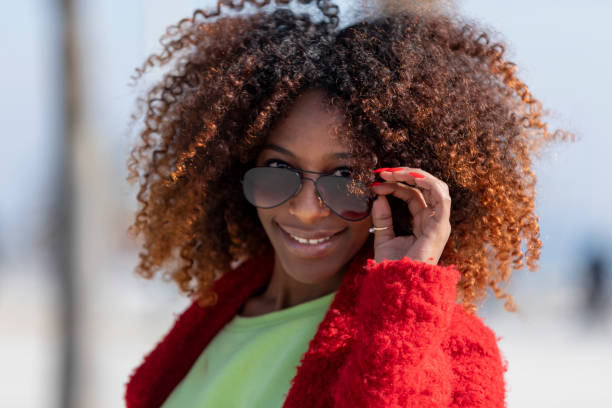istock Front view of a young beautiful curly woman standing on path smiling while looking camera in sunny day 1129153417