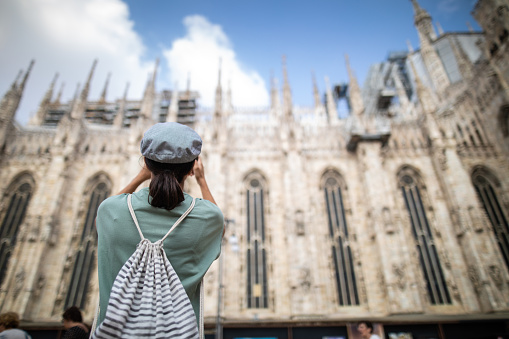 Rear view of unrecognizable woman taking photos in front of Duomo Cathedral on beautiful day, low angle view