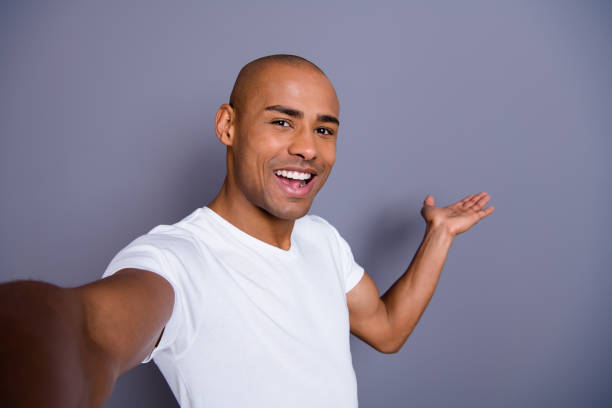 cerrar piel oscura masculino sano de la foto que le su cabeza calva macho hacer tomar autorretratos traducción video blog show para extranjeros usar blanco camiseta equipo ropa aislado fondo gris - video conference camera fotografías e imágenes de stock