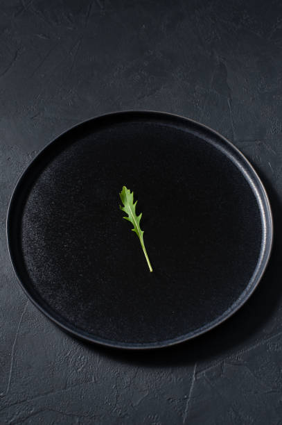 istock Arugula on a black plate, minimalism, concept. Dark background, top view 1129155637