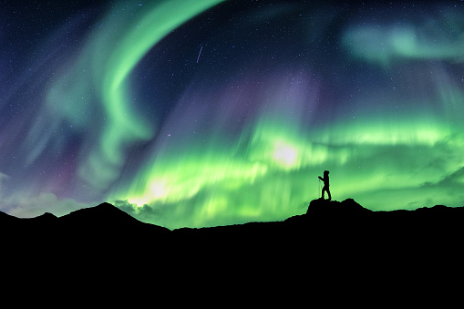 Man hiking on mountain with northern lights explosion at norway