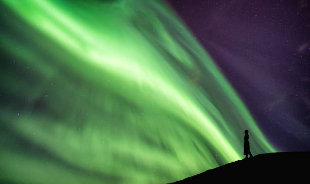 istock Silhouette woman standing on cliff with aurora borealis dancing on sky 1129156493