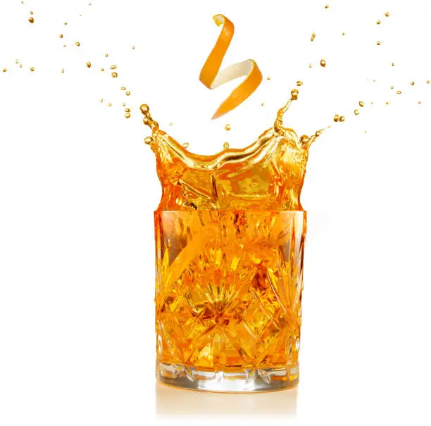 orange zest falling into a splashing cocktail isolated on white