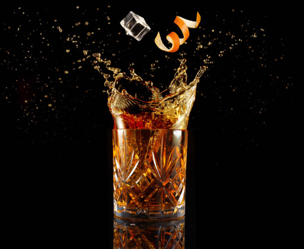 cocktail splashing isolated on black orange zest and ice falling into splashing cocktail isolated on black amber black photography stock pictures, royalty-free photos & images