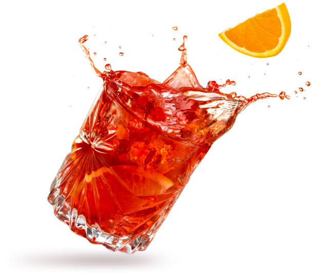 splashing negroni cocktail isolated on white orange slice falling into a splashing negroni tilted on white background red drink stock pictures, royalty-free photos & images