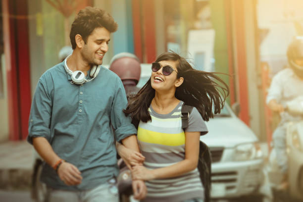 Candid image of Asian, Indian happy young couple walks together by hand in hand on city road in outdoor market at day time.