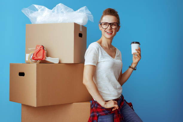 istock smiling modern woman near cardboard box with coffee cup on blue 1129167885