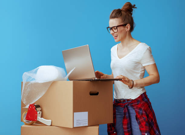 istock happy young woman near cardboard box using laptop on blue 1129170747