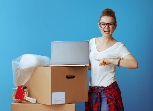 istock woman near cardboard box pointing laptop blank screen on blue 1129170886