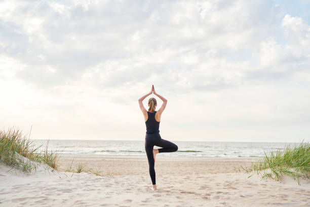 mujer joven haciendo yoga en la playa - yoga fotos fotografías e imágenes de stock