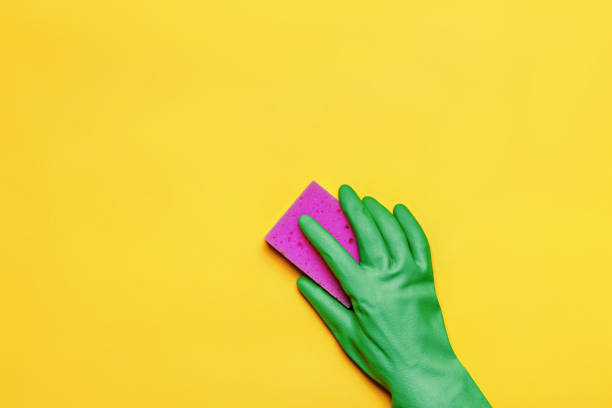 A hand in a rubber protective glove with a pink sponge on a yellow background. Cleaning concept.