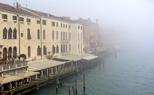 View from the bridge Ponte degli Scalzi in the Grand Canal in Venice on a cold and foggy winter day. In the foreground are some restaurants to see.