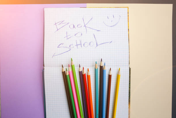 istock Color pencils lying on pastel purple and beige background. Squared notebook with back to school concept sign and smile. Colorful art studying and painting. Copy space place for postcard wish. 1129187784