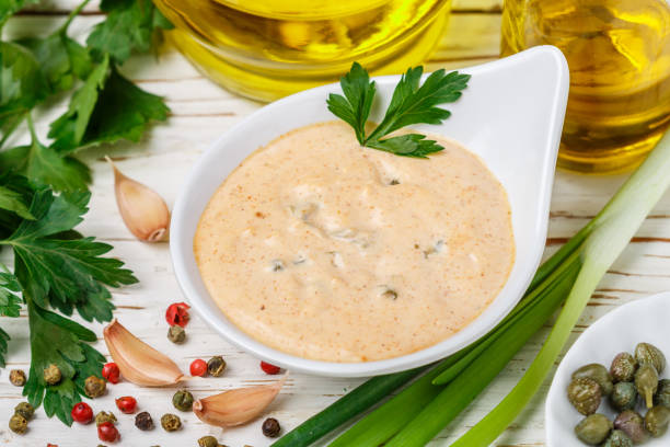 homemade traditional french remoulade sauce in a white bowl with ingredients-capers, parsley, green onion, mustard, fragrant vinegar, olive oil, garlic on a light wooden table. dip. selective focus - caper sauce imagens e fotografias de stock