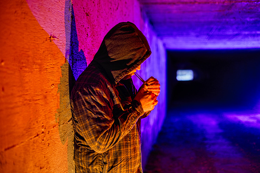 Criminal Drug Addict Smoking Drugs in Underground Tunnel - Man smoking drugs out of glass pipe in underground urban setting. Poverty, crime and homeless drug addiction theme.