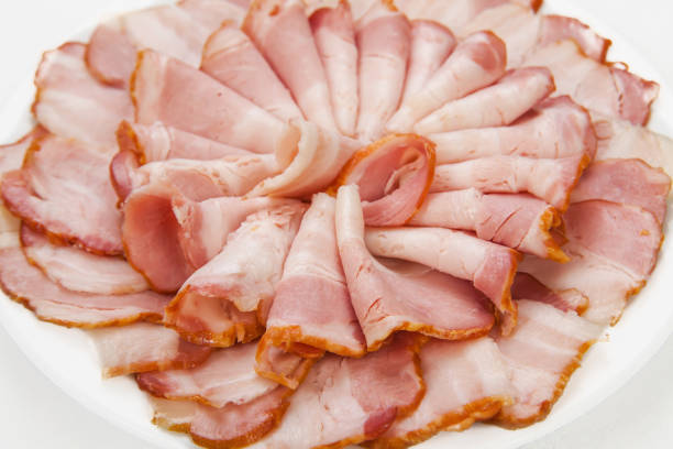 Sliced meat, bacon pieces on a white plate. Isolated on white background. Snack. Meat dish. Closeup