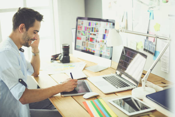 istock Portrait of young designer sitting at graphic studio in front of laptop and computer while working online 1129196991
