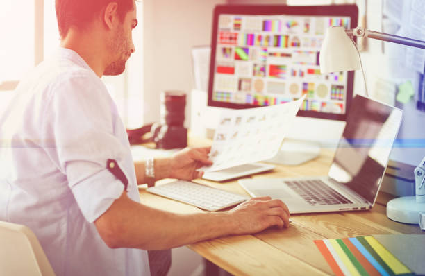 istock Portrait of young designer sitting at graphic studio in front of laptop and computer while working online 1129196994