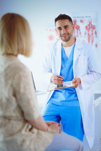 istock Handsome doctor is talking with young female patient and making notes while sitting in his office 1129197066