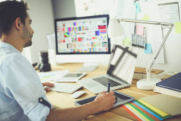 istock Portrait of young designer sitting at graphic studio in front of laptop and computer while working online 1129197164
