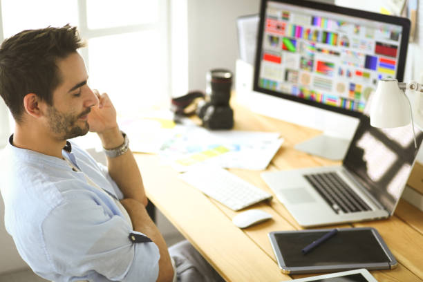 istock Portrait of young designer sitting at graphic studio in front of laptop and computer while working online 1129197178
