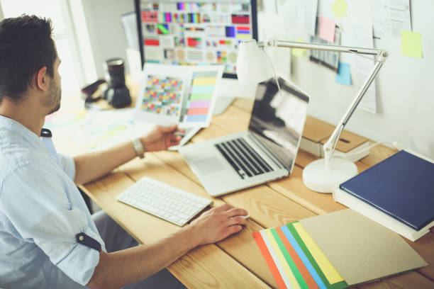 istock Portrait of young designer sitting at graphic studio in front of laptop and computer while working online 1129197183