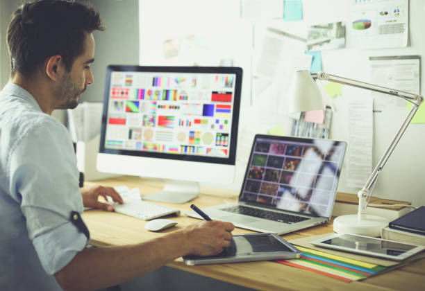 istock Portrait of young designer sitting at graphic studio in front of laptop and computer while working online 1129197191