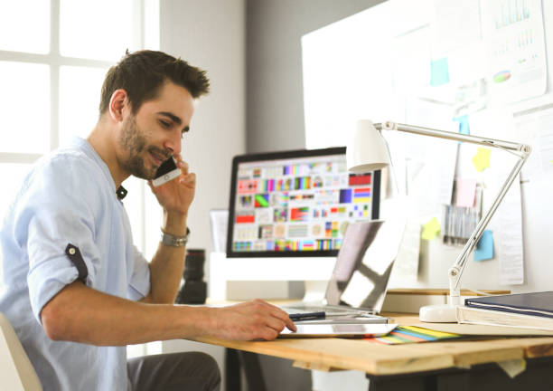 Portrait of young designer sitting at graphic studio in front of laptop and computer while working online