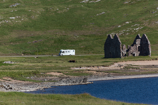 Motorhome driving along an old ruin of a house at Loch Assynt in the Scottish Highlands, Scotland