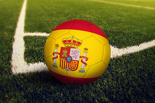 Spain ball on corner kick position, soccer field background. National football theme on green grass.