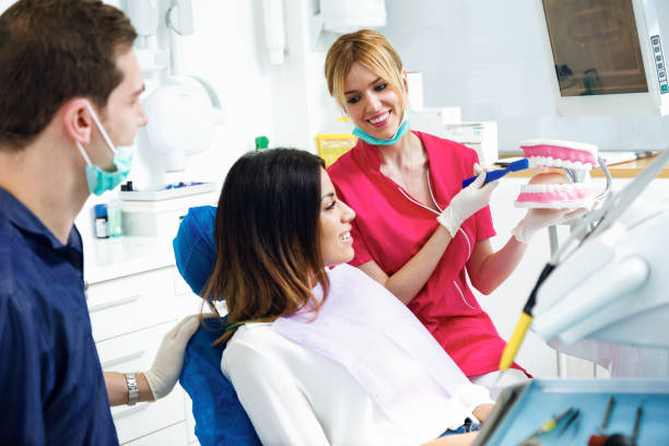 istock Beautiful dentist explaining how to brush teeth correctly to a patient in a clinic box with medical equipment. 1129202893