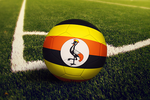 Uganda ball on corner kick position, soccer field background. National football theme on green grass.