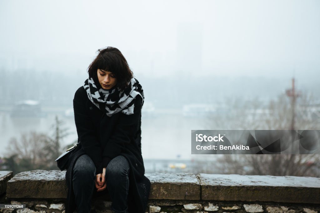 Girl, alone. Girl sitting on a wall and having a tough time Seasonal Affective Disorder Stock Photo