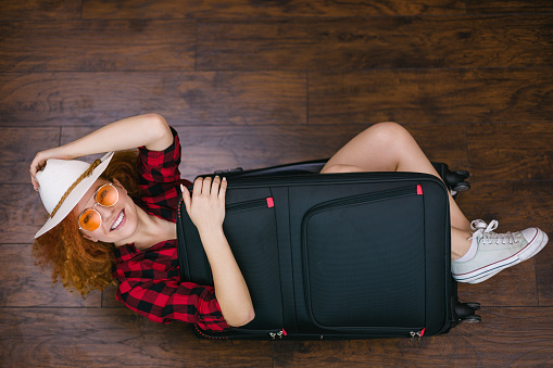 Beautiful young girl with long red curly hair packing suitcase for a holiday. Travel concept