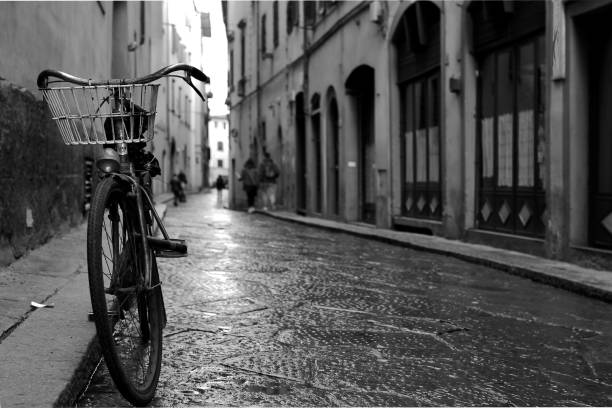 Florence, Italy - March 13, 2018. A bicycle and some unrecognizable people. The bicycle is leaning against the wall. people move in the distance. the photo is black and white.