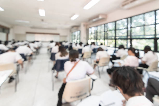 istock Blur school student exam background  in university class with blurry view from back of the classroom of young people having stress doing examination admission test in classroom for education 1129246830