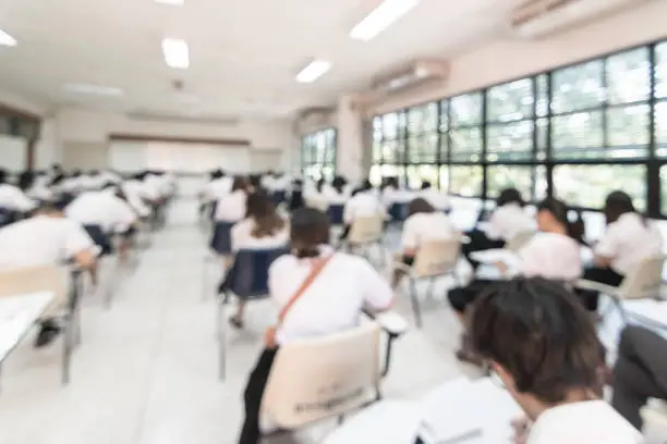 Photo of Blur school student exam background  in university class with blurry view from back of the classroom of young people having stress doing examination admission test in classroom for education