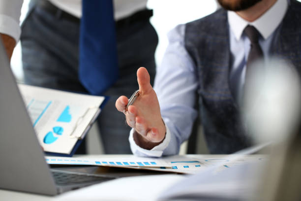 istock Group of businessmen point arm with silver pen at laptop pc 1129246896