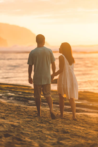 istock A striking Eurasian couple holds hands as they walk along the beach at sunset 1129246965