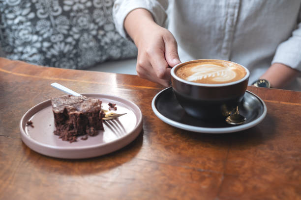istock a woman's hand holding and drinking hot latte coffee with brownie cake on the table 1129256906
