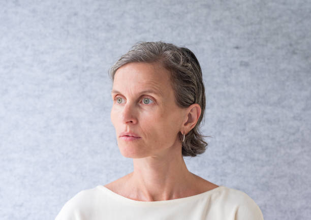 istock Middle aged woman in cream top against grey background 1129277145